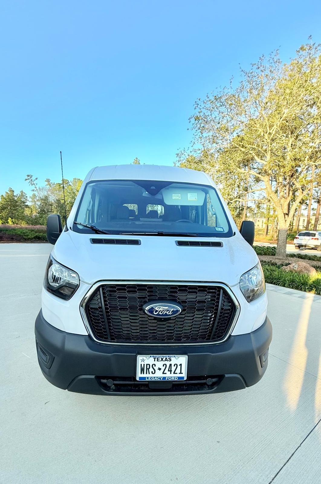 White Ford Transit van parked in lot with trees in background